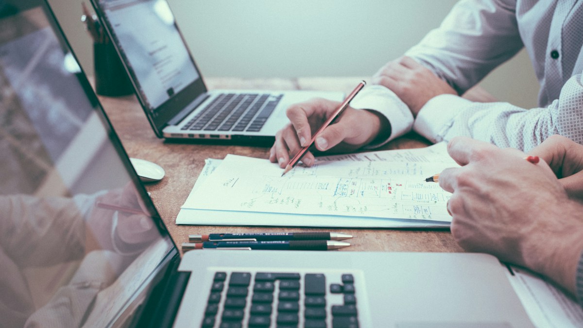 A person holding a pencil near a laptop and paperwork